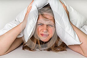 Woman in bed covering ears with pillow because of noise