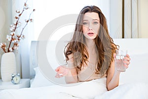 Woman in bed holding pills and glass of water