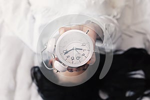 Woman In Bed Holding Up An Analog Alarm Clock Showing 7:00 am