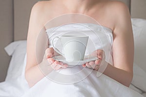Woman in bed holds a white cup on a saucer in her hands