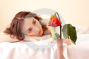 Woman in bed looking on the rose (focus on rose)