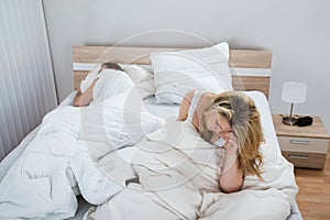 Woman on bed while man sleeping in bedroom