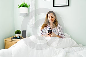 Woman in bed smiling while texting on her phone