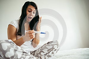 Woman in bed surprised by pregnancy test