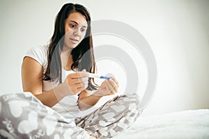 Woman in bed surprised by pregnancy test
