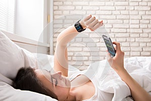 Woman On Bed Synchronizing Smart Watch With Cell Phone