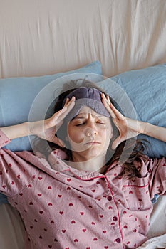 woman in bed wakes up, insomnia and sleep disorder. person in sleep mask holds his head and face