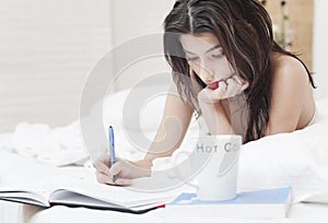 Woman in bed writing on a notebook