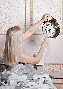 The woman in the bedroom with a large alarm clock in his hand shows the time of awakening.