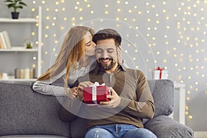 Woman from behind hugs and kisses her beloved husband giving him a gift on this special day.