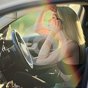 The woman behind the wheel is painting her eyelashes. Blond woman in the car applying makeup