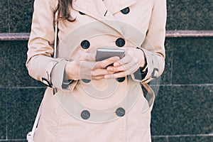 Woman in a beige coat holds a mobile phone in hands