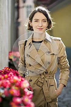 Woman at beige coat smile surrounded by flowers