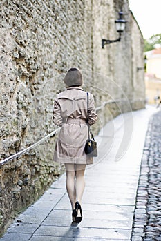 Woman at beige coat walks along the wall