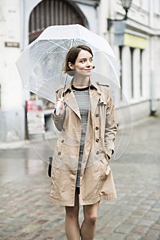 Woman at beige coat walks at wet street