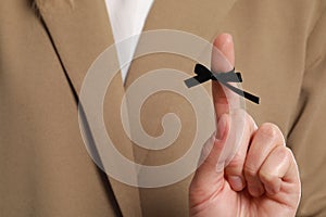 Woman in beige suit showing index finger with tied black bow as reminder, closeup