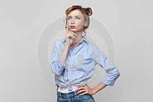 Woman being deep in thoughts, raises holding chin, looking up with thoughtful expression.