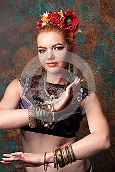 Woman in belly dance costume with black lace in red circlet of flowers looking at camera and holding hands near chest in tribal po