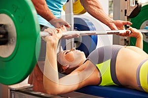 Woman bench pressing weights with assistance of trainer