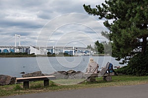 A Woman on a bench sitting alone. Bridge and Lake background.