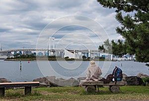 A Woman on a bench sitting alone. Bridge and Lake background.