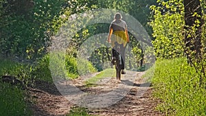 Woman on Bicycle Rides Along Green Forest Path on Sunny Summer Day, Slow Motion