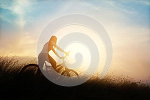 Woman with bicycle on a rural road with grass sunset background