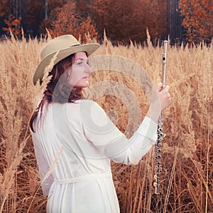 A woman with big flute boehm stands in autumn grass, yellow field