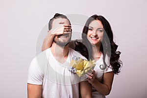 Woman with big toothy smile holding boyfriends eyes giving him a present for Valentine's day.