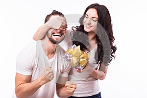 Woman with big toothy smile holding boyfriends eyes giving him a present for Valentine's day.