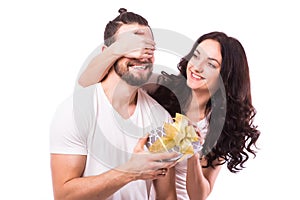 Woman with big toothy smile holding boyfriends eyes giving him a present for Valentine's day.