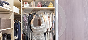 Woman in big walkin closet choosing clothes. modern wardrobe and dressing room with copy space