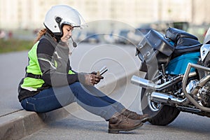 Woman biker trying to find road with sat nav while sitting on roadside near motorcycle