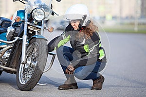 Woman biker trying to repair flat tire on motorcycle at city asphalt road