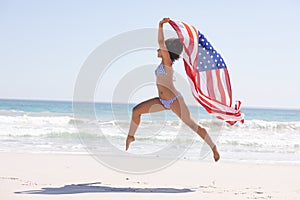 Woman in bikini with american flag jumping on the beach