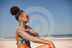 Woman in bikini applying sunscreen lotion on shoulder at beach in the sunshine