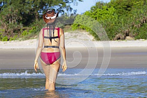 Woman and bikini crimson with hat walk on beach