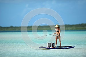 Woman in bikini fishing and paddle boarding