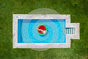 A woman in bikini floats on a watermelon shaped float in a pool