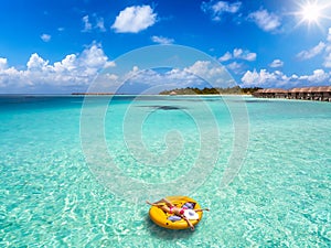 A woman in bikini and with hat relaxes on a round float over the turquoise sea of the Maldives