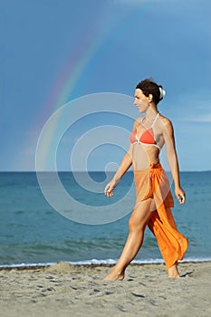 Woman in bikini and pareo walking on beach