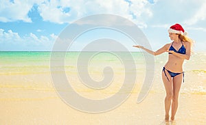 Woman in bikini with red christmas santa claus hat pointing at ocean beach view