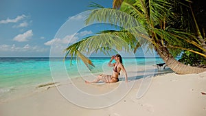 Woman in bikini relaxes in shade of palm tree near ocean