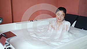 Woman in bikini relaxing with foam bath inside bathtub