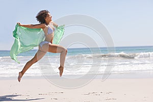 Woman in bikini with scarf jumping on the beach