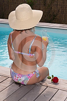 Woman in bikini sitting front pool and drinking cocktail,
