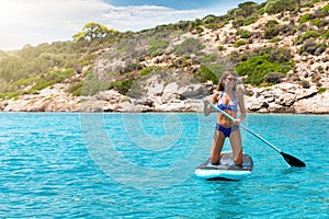 Woman in a bikini on a stand up paddle board over turquoise, Mediterranean waters