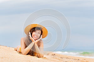 woman in a bikini and a straw hat lies on a tropical beach. Beautiful girl lying and smiling on the sand while