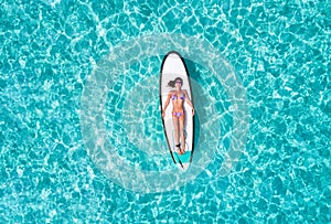 Woman in bikini is sunbathing on a surfboard