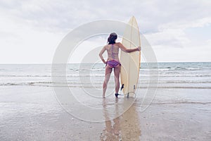 Woman in bikini with surfboard on beach